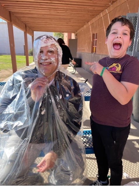 Mason celebrates reaching his I-Ready milestones by throwing a pie at Sierra School of Gilbert Director Mr. Matt, with both smiling after the fun moment.