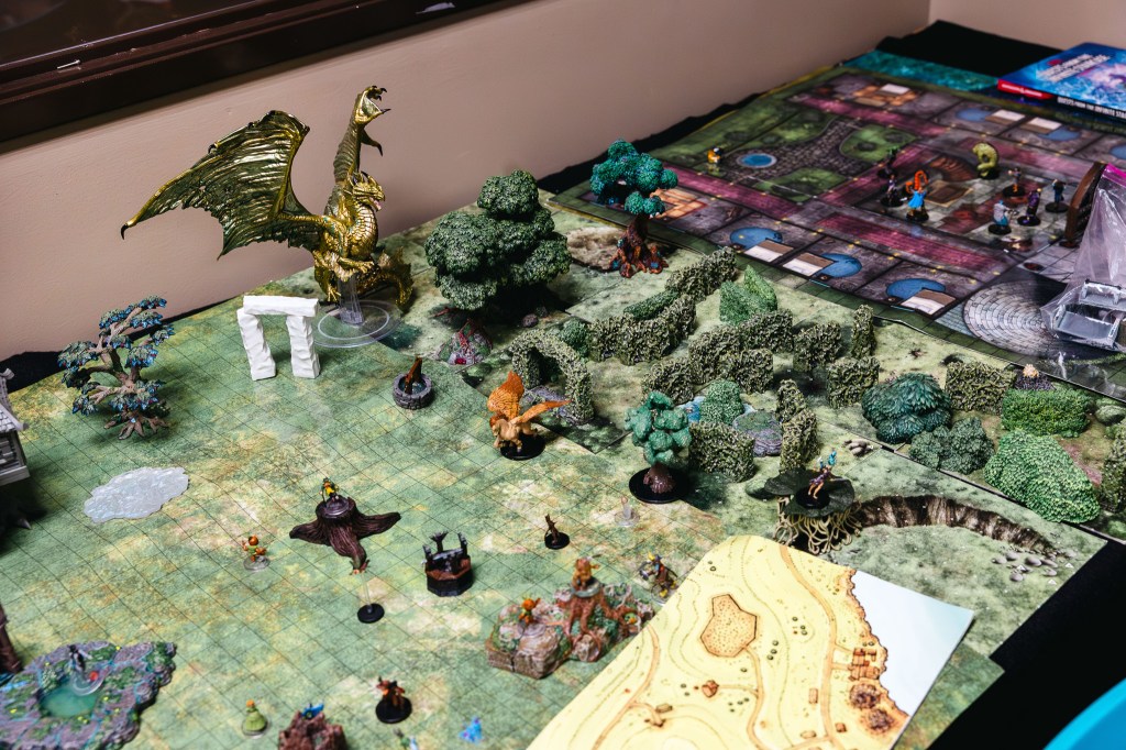 Tabletop role-playing game setup with fantasy miniatures, terrain, trees, and a dragon