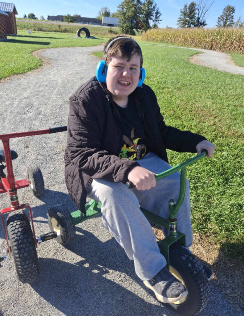 Student wearing headphones rides a tricycle during the High Road School of Bucyrus field trip at The Pickwick Place, enjoying accessible outdoor activities.