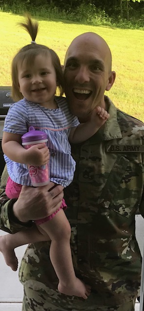 Veteran educator Vincent Lindsley in military fatigues holding his child