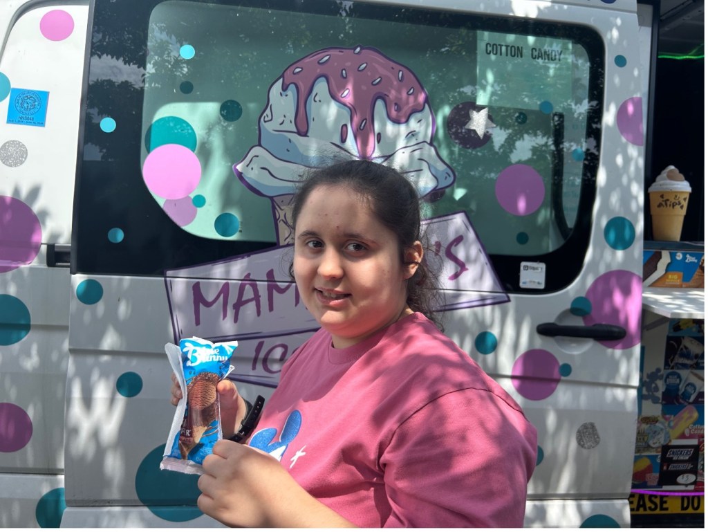 Kristina smiling at the camera while holding an ice cream treat in front of an ice cream van during a school outing at BEST Academy.