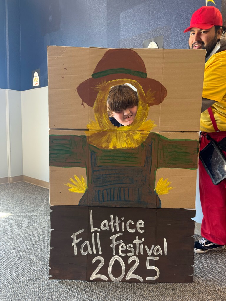 Student posing through painted scarecrow photo board at Lattice Fall Festival 2025.