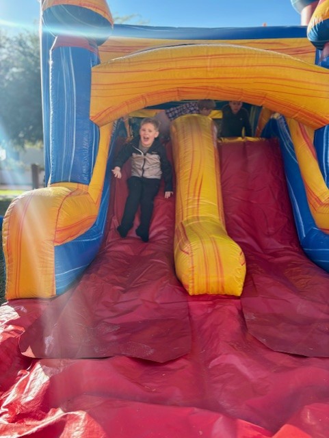 Estudiante sonriendo mientras se desliza por un castillo hinchable en el Carnaval de Invierno.