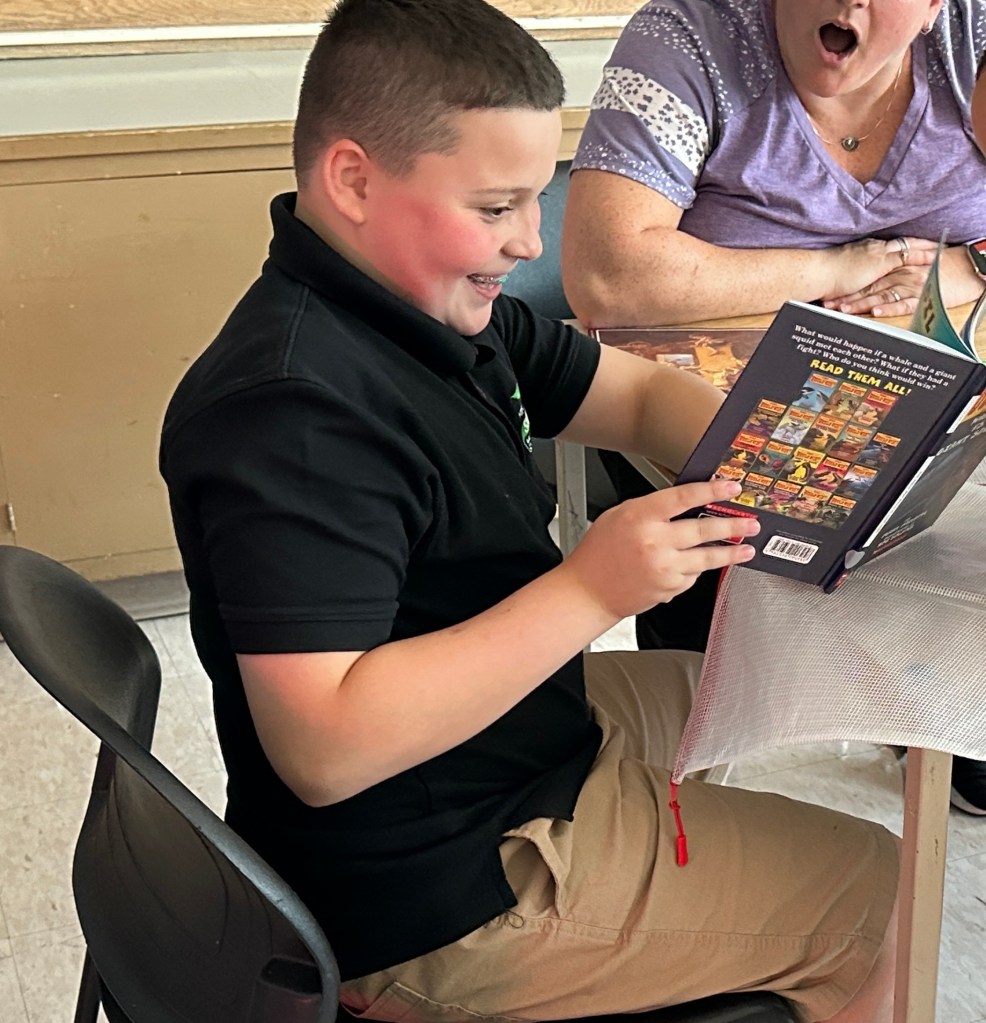 Aiden smiling with a book during student progress at High Road School