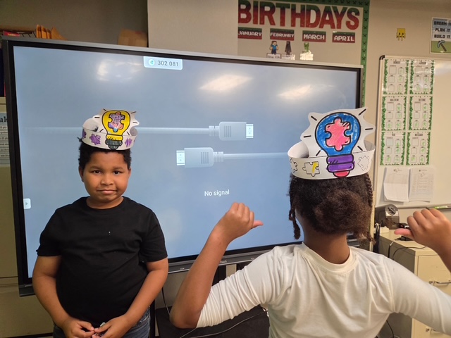 Unos alumnos, con gorros de papel que representan el pensamiento, se señalan la cabeza mientras participan en una actividad de sensibilización sobre el autismo en el aula