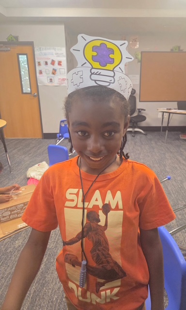 Un alumno posa con un gorro de papel que simboliza el pensamiento mientras aprende sobre la sensibilización hacia el autismo y la inclusión en el aula