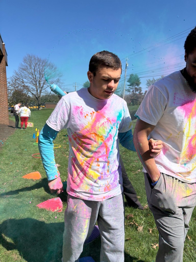 Student receives support from staff during color walk activity with obstacle course in background