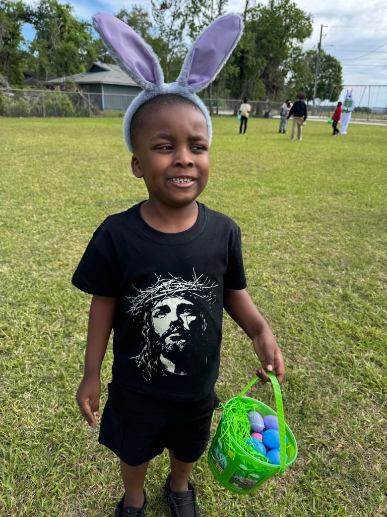 Student wearing bunny ears holding eggs with Easter Bunny in background