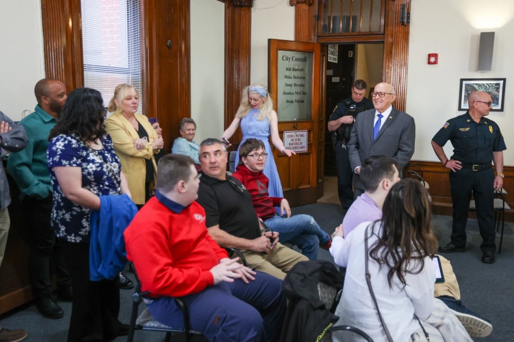 Cathy Payne, secretaria del Ayuntamiento de Wilkes-Barre, ayuda al miembro honorario del Ayuntamiento Jaxon Gillam a colocarse la banda durante un acto celebrado con motivo del Mes de Concienciación sobre el Autismo en el Ayuntamiento de Wilkes-Barre el viernes 10 de abril de 2026.