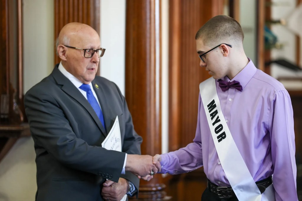 Cathy Payne, secretaria del Ayuntamiento de Wilkes-Barre, ayuda al miembro honorario del Ayuntamiento Jaxon Gillam a colocarse la banda durante un acto celebrado con motivo del Mes de Concienciación sobre el Autismo en el Ayuntamiento de Wilkes-Barre el viernes 10 de abril de 2026.