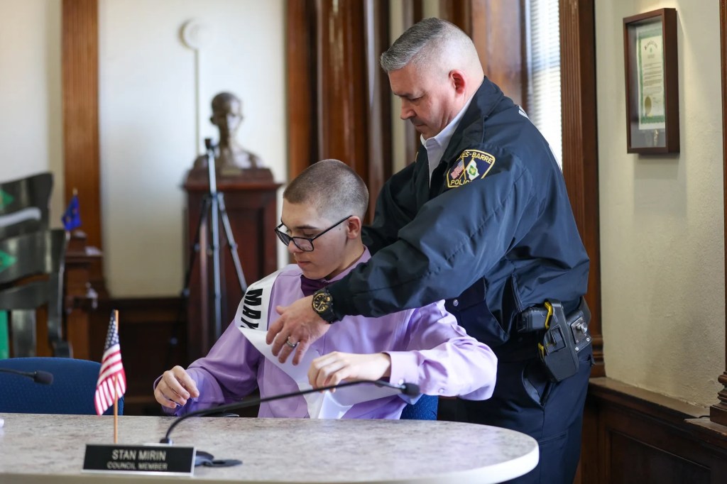 Cathy Payne, secretaria del Ayuntamiento de Wilkes-Barre, ayuda al miembro honorario del Ayuntamiento Jaxon Gillam a colocarse la banda durante un acto celebrado con motivo del Mes de Concienciación sobre el Autismo en el Ayuntamiento de Wilkes-Barre el viernes 10 de abril de 2026.