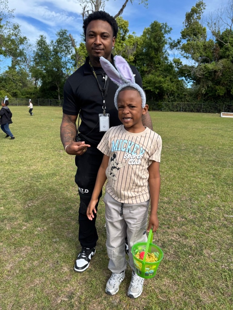 Student with bunny ears smiling with staff during egg hunt