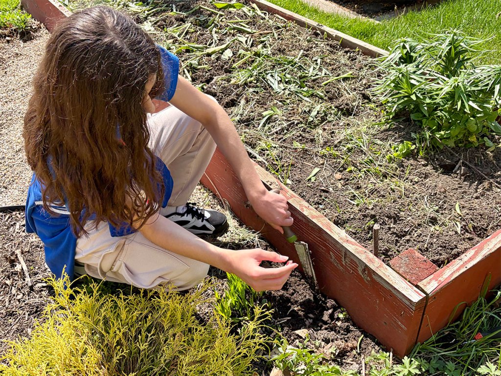 Un alumno planta en un bancal elevado durante el Día de la Tierra en la NewHope Academy