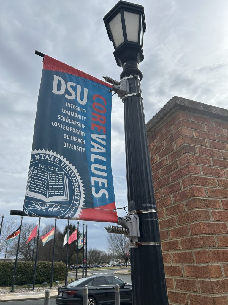 Cartel de la Universidad Estatal de Delaware en un poste de luz del campus en el que se indica el año de fundación, 1891, y los valores fundamentales, entre los que se incluyen la integridad y la excelencia académica