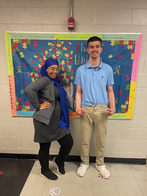 Student and staff smiling together in front of an autism awareness display at Delco Academy