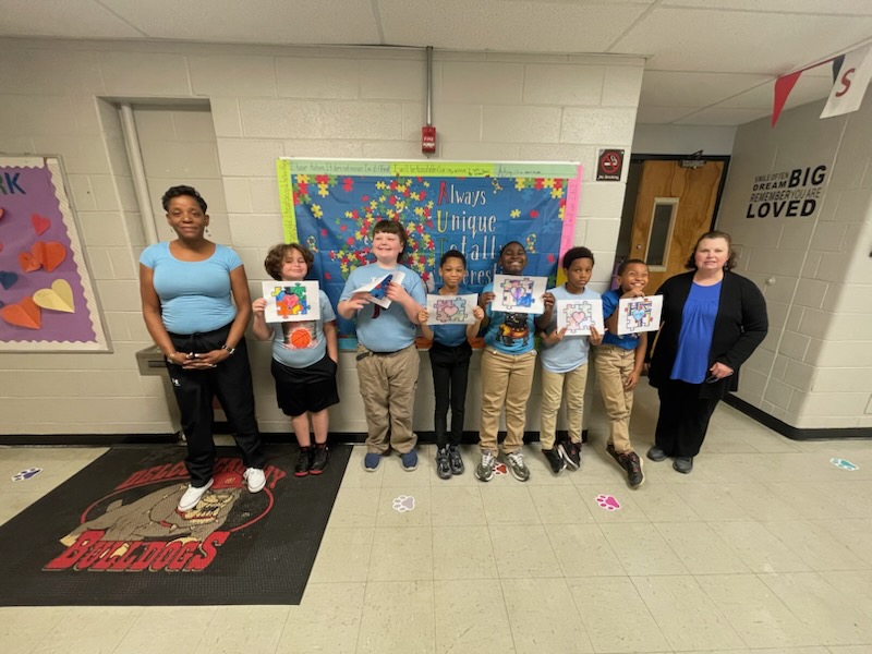 Students holding up artwork alongside staff during autism awareness activities at Delco Academy