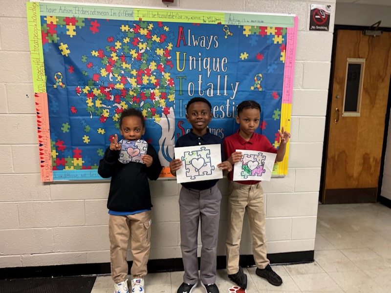 Students displaying their artwork in front of an autism awareness sign at Delco Academy