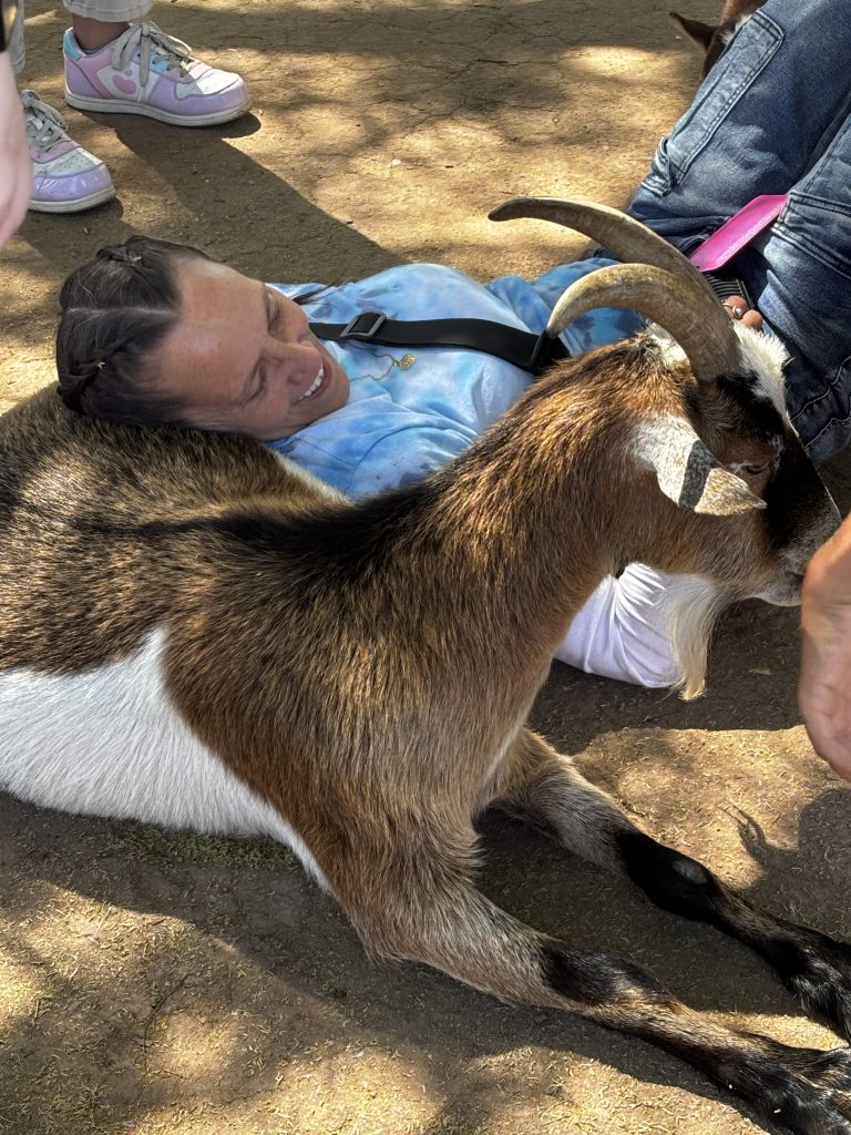 Un miembro del personal descansando junto a una cabra en una feria de sensibilización sobre el autismo