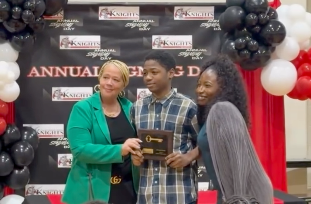 Alumnos y personal posando con el premio durante la jornada de firma de contratos en la Excel Middle Years Academy