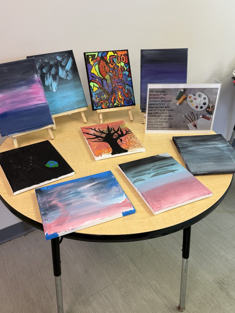 Table displaying multiple student canvas paintings at High Road School art show