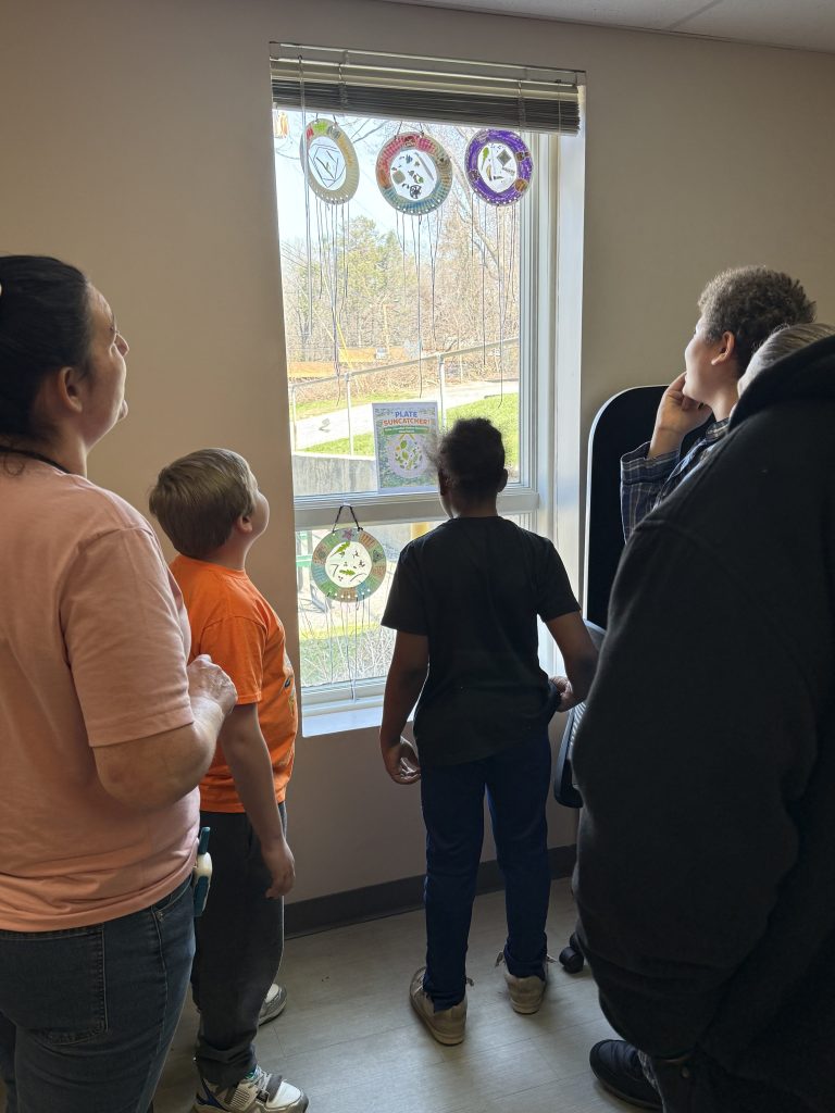 Students and staff viewing paper plate suncatcher art on window