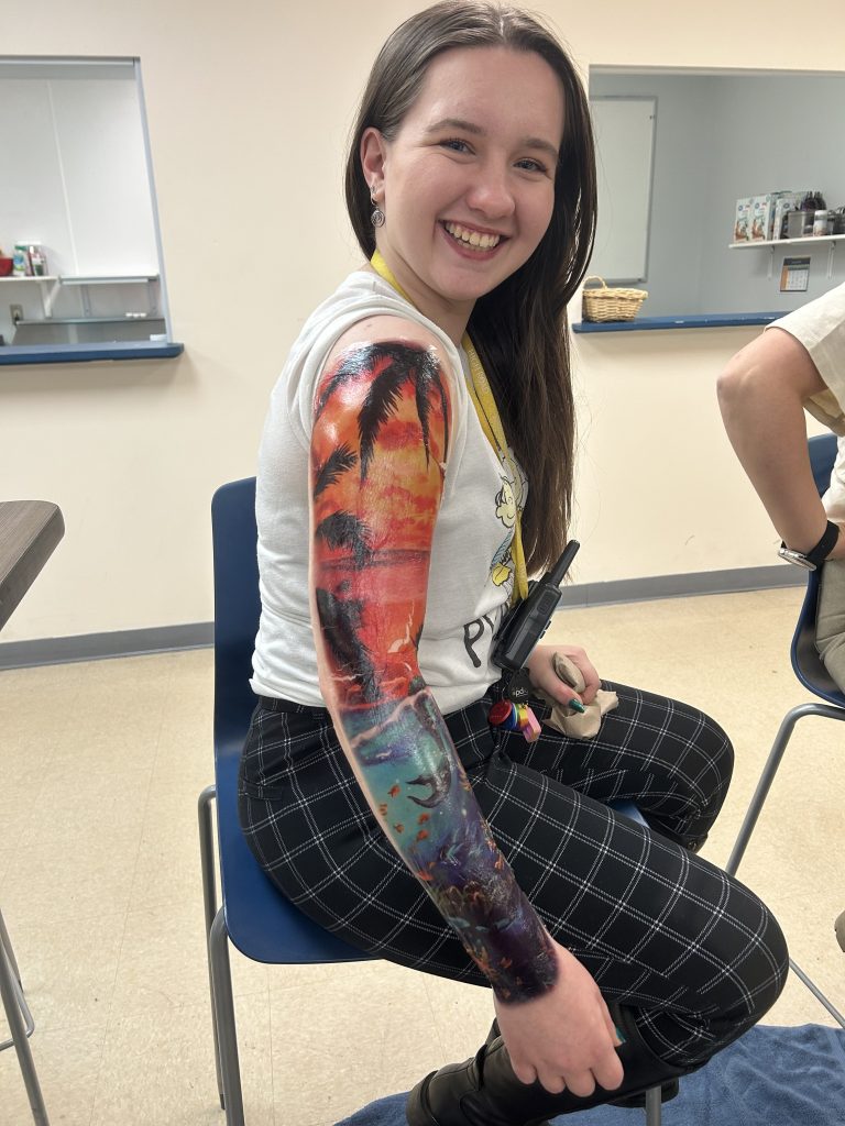 Staff member smiling and showing arm covered in temporary tattoos