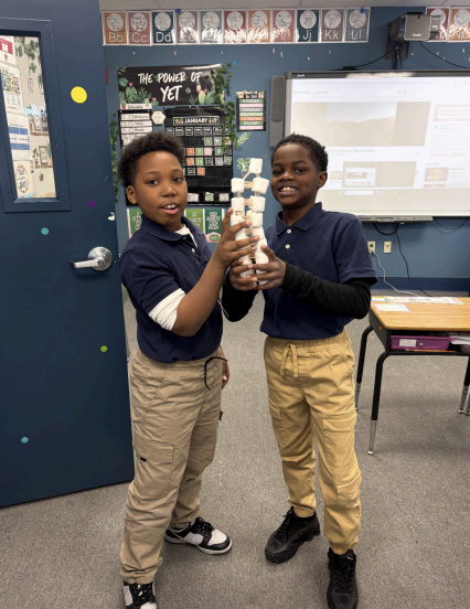 Two students smiling while holding up their completed tower in classroom activity
