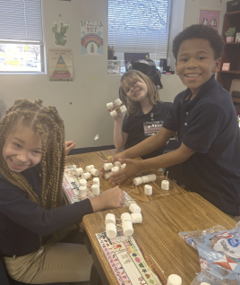 Three students working together on tower building project and smiling at camera