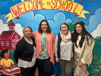 Four staff members stand together in front of a welcome mural inside High Road School of Wallingford during Social Work Month