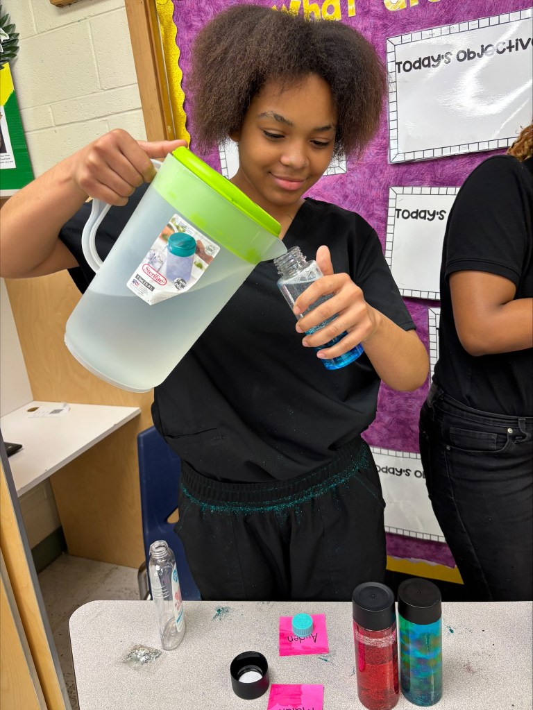 Un alumno sonríe mientras vierte agua en una botella sensorial durante un proyecto de apoyo al autismo