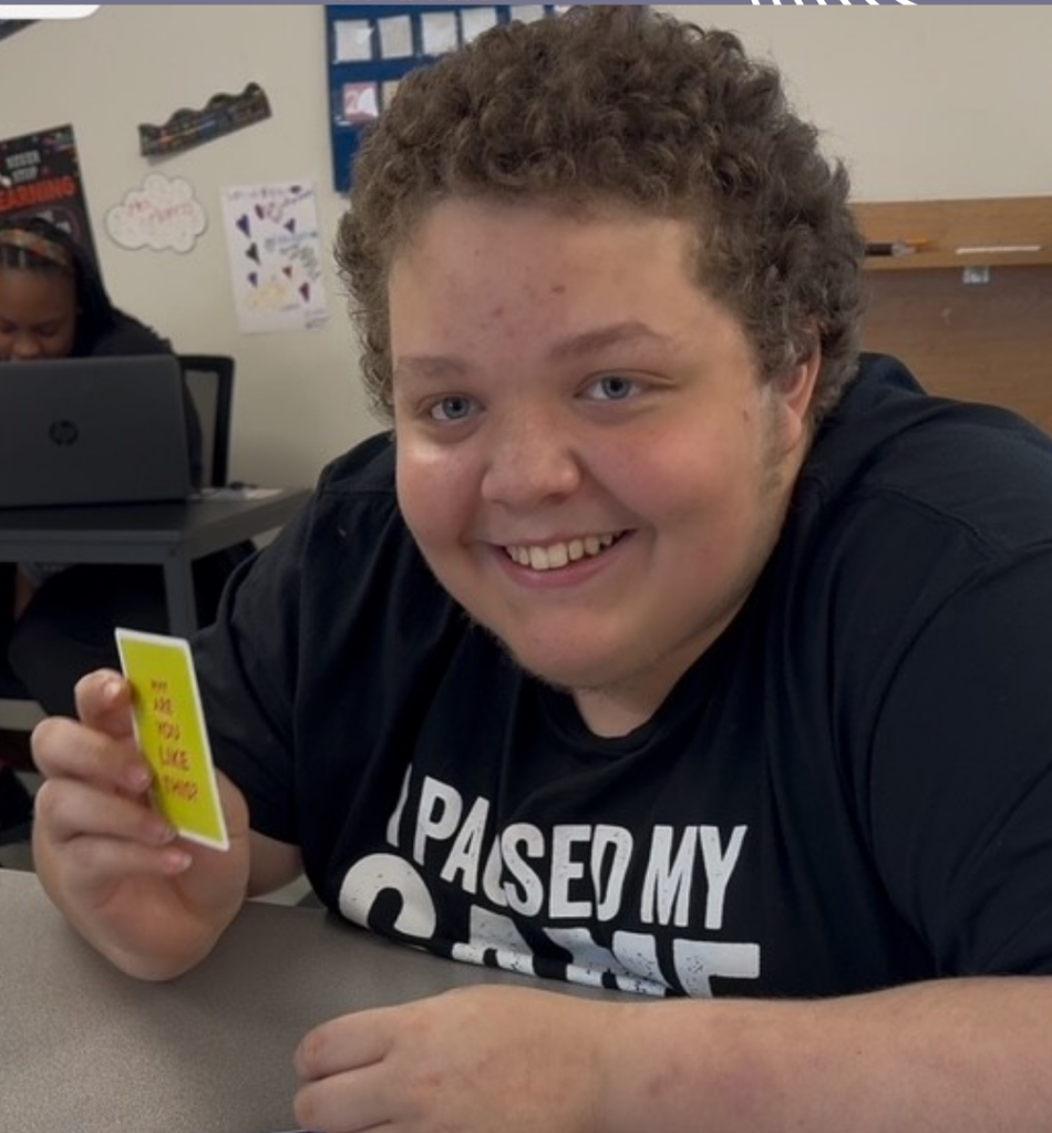 Christian smiling and holding a card during a classroom moment at Sierra School at Wylie