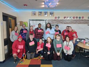 Un grupo de alumnos y personal posando en un aula con un cartel en el que se lee: «NWCA, estamos orgullosos de nuestro colegio».