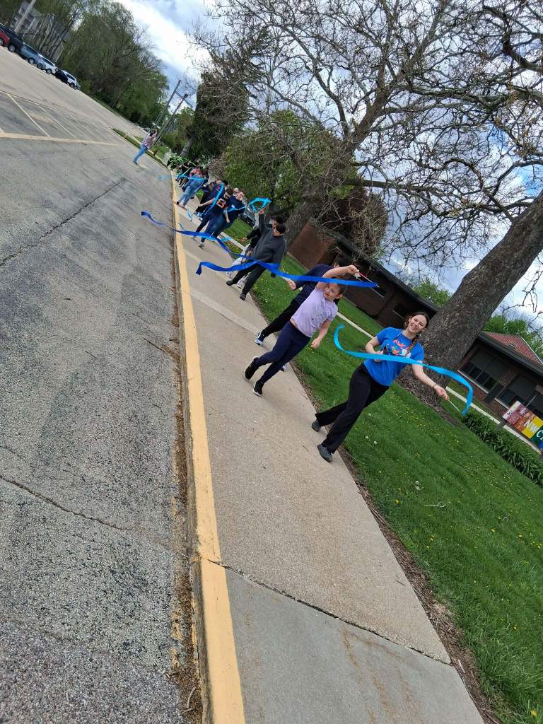 Estudiantes y personal participan en una marcha del arcoíris portando banderas de papel azules y verdes durante una celebración comunitaria.