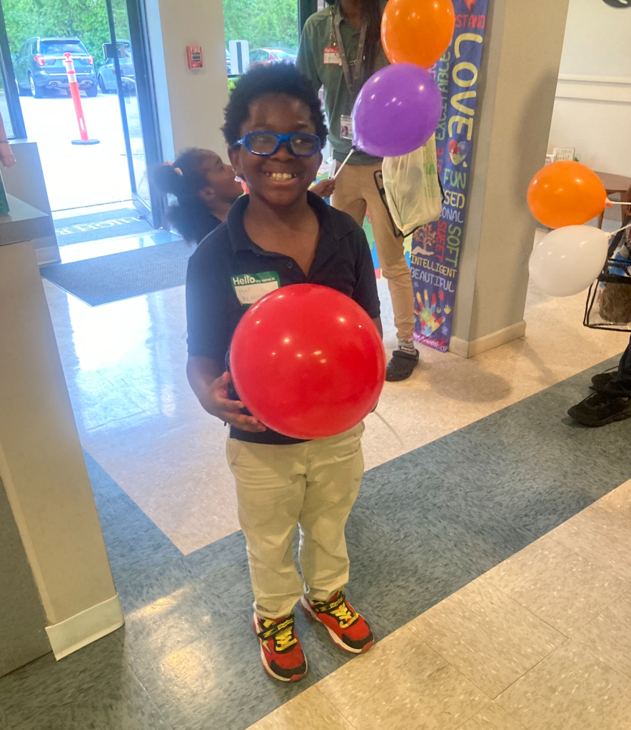 Student smiles while holding a red balloon during the family resource event at High Road School of Anne Arundel County.
