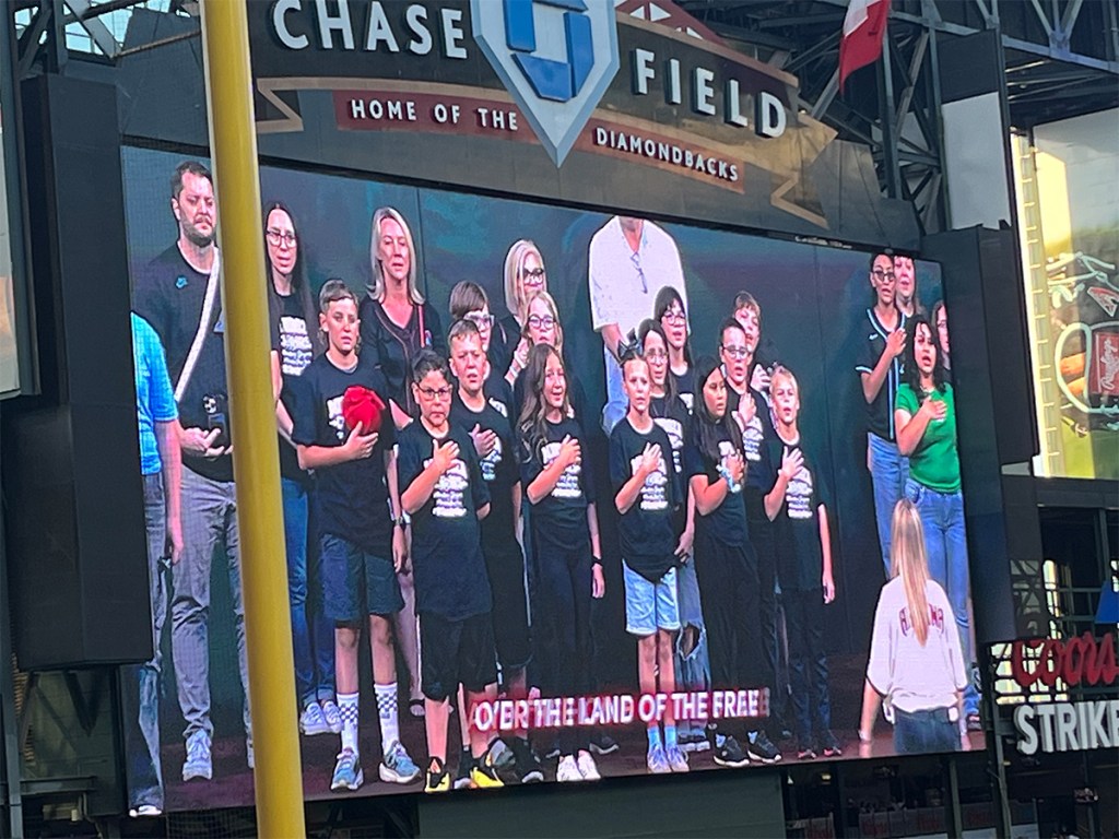 Fans stand for the national anthem as displayed on the stadium video board at Chase Field.