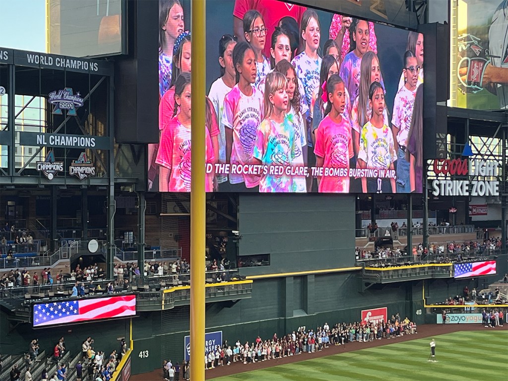 Photo 7: Students in tie-dye shirts appear on the stadium video board during the national anthem before the game.