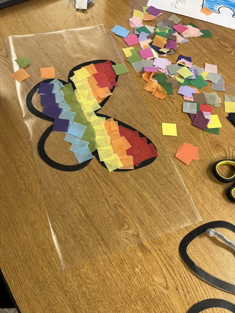 Butterfly-themed craft materials spread across a table with colorful paper squares, scissors, and art supplies.