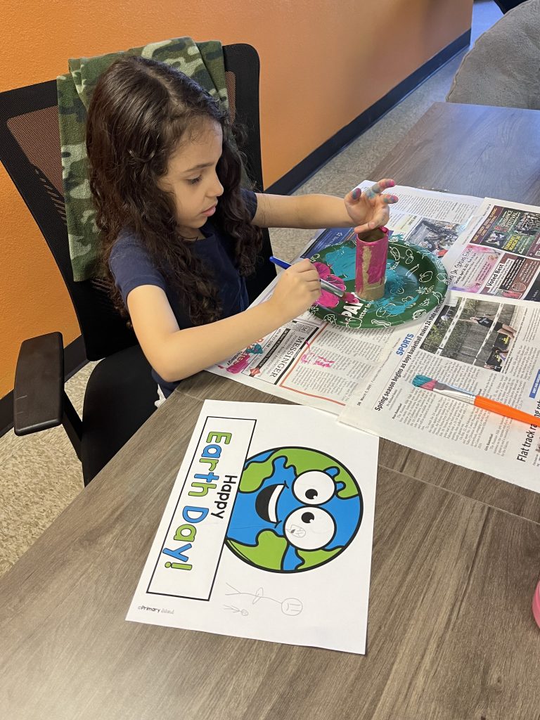 Student painting with a cardboard tube and paintbrush during a hands-on Earth Day craft activity in the classroom.