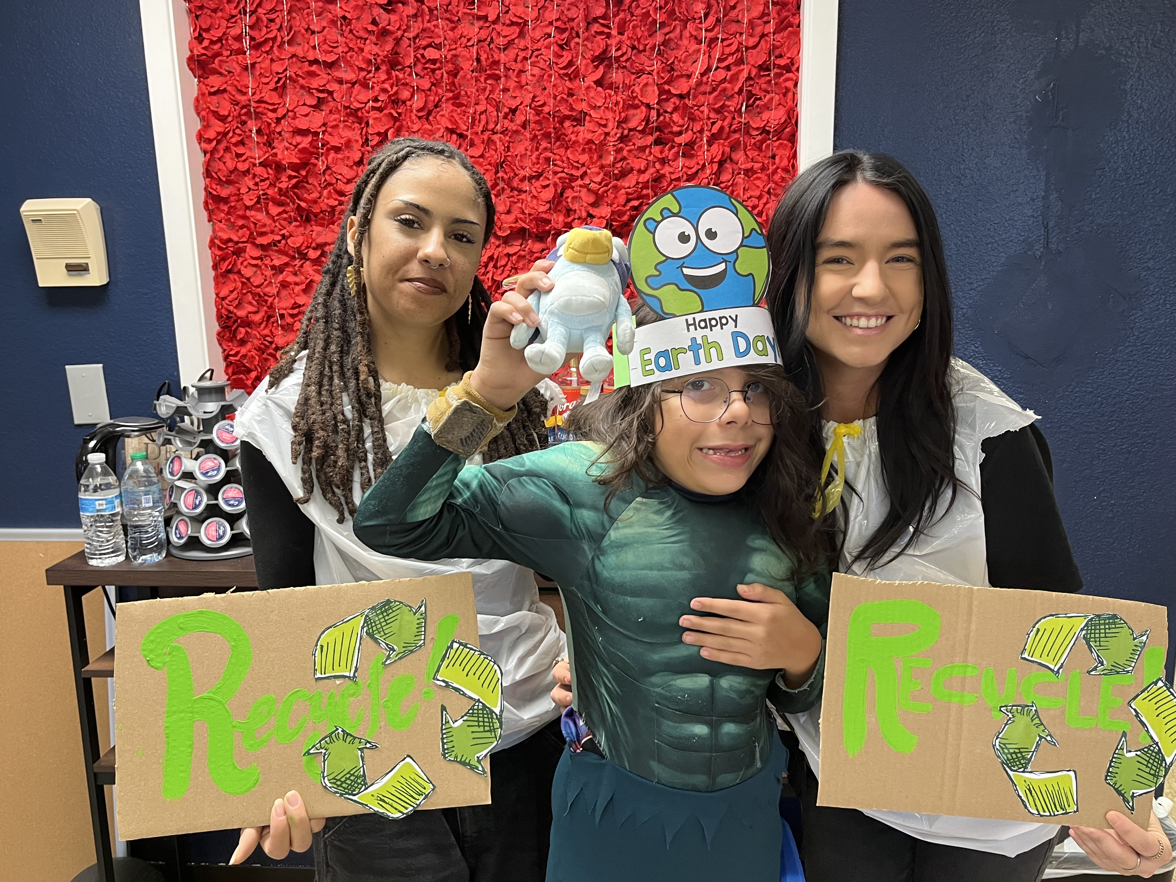Staff members and student smiling while holding handmade recycling signs and Earth Day crafts at Sierra School of Scottsdale.