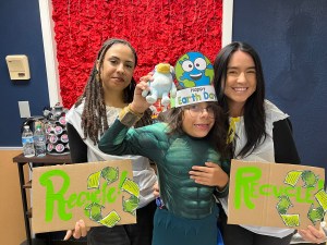 Staff members and student smiling while holding handmade recycling signs and Earth Day crafts at Sierra School of Scottsdale.