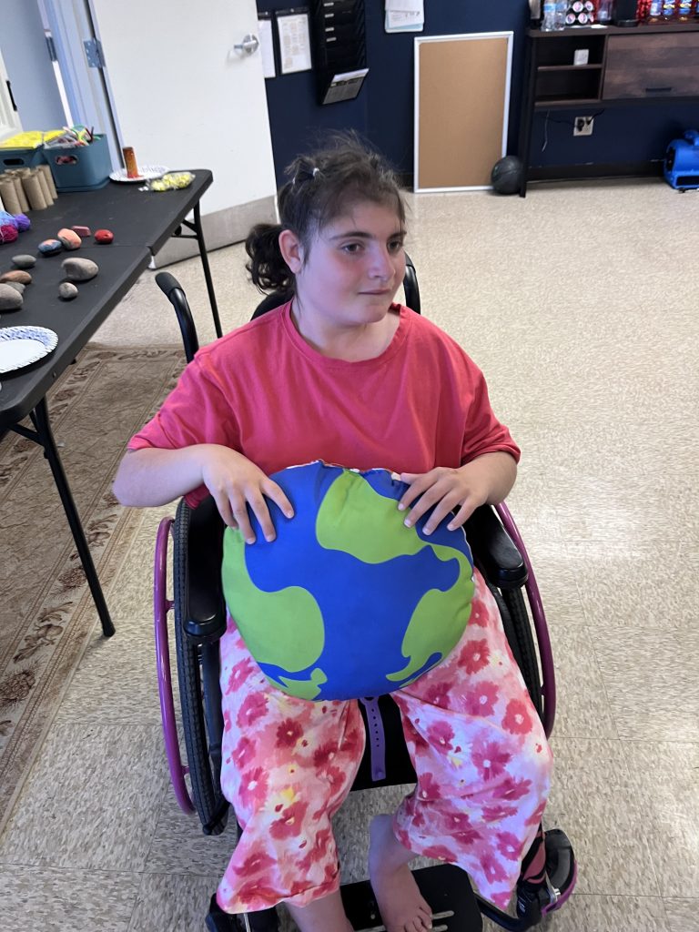 Student sitting in a wheelchair holding a globe-themed pillow during classroom activities celebrating Earth Day and inclusion.