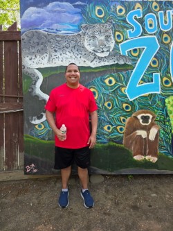 Vaughn smiling in front of a colorful animal mural during a school field trip to Southwick Zoo.