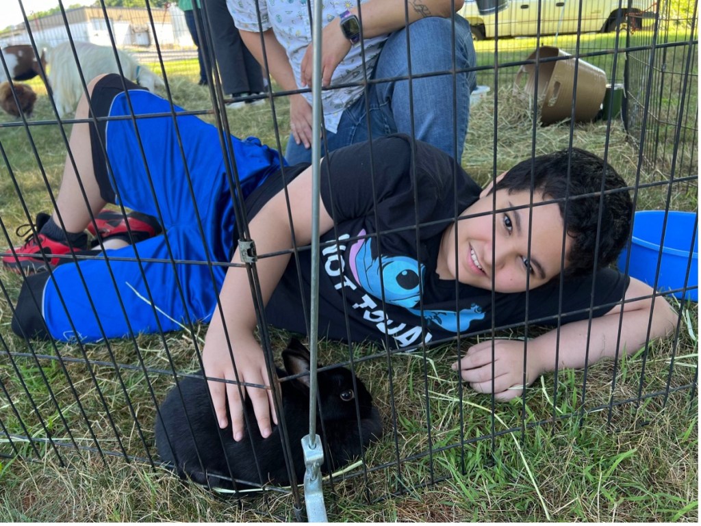 Un alumno tumbado en la hierba mientras acaricia suavemente a un conejito negro durante una actividad al aire libre en la Academia B.E.S.T.