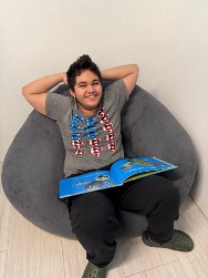 Un estudiante relajado en un puf, con un libro abierto sobre el regazo y una sonrisa en el rostro, en el aula