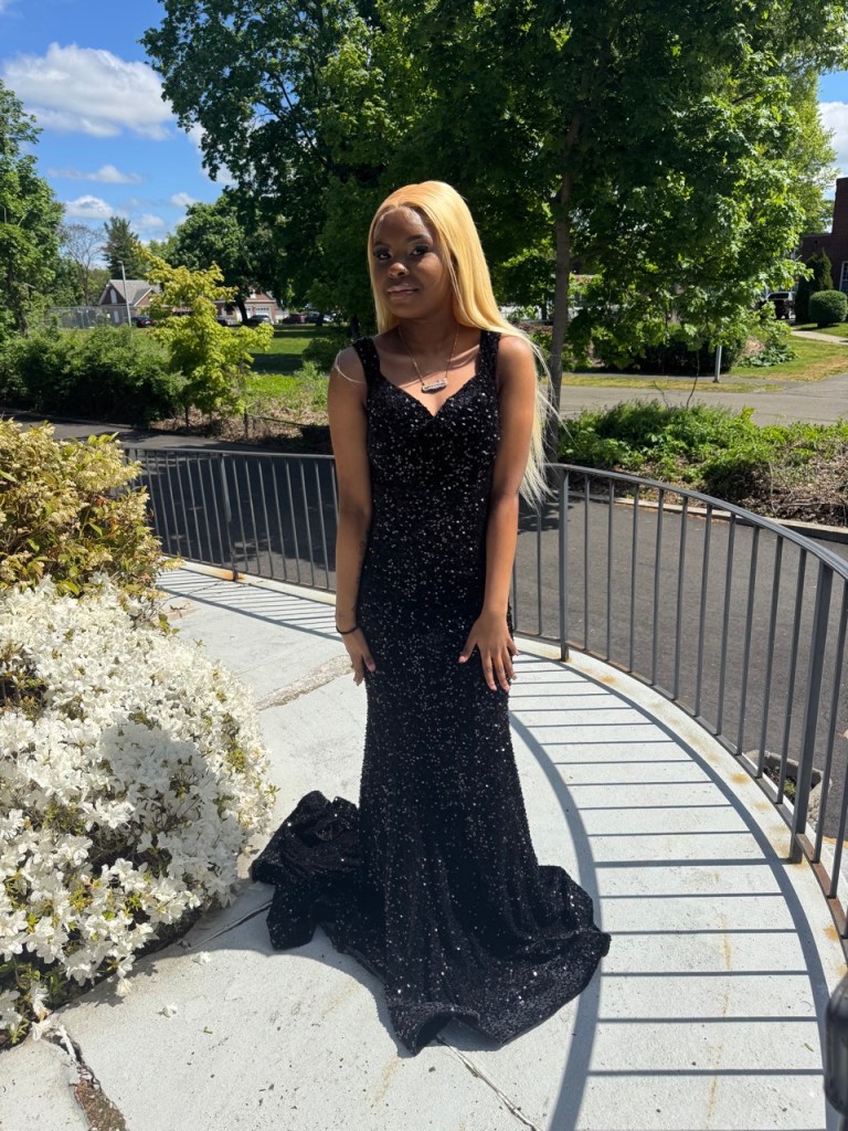 Una estudiante posa al aire libre con un vestido de gala negro con lentejuelas