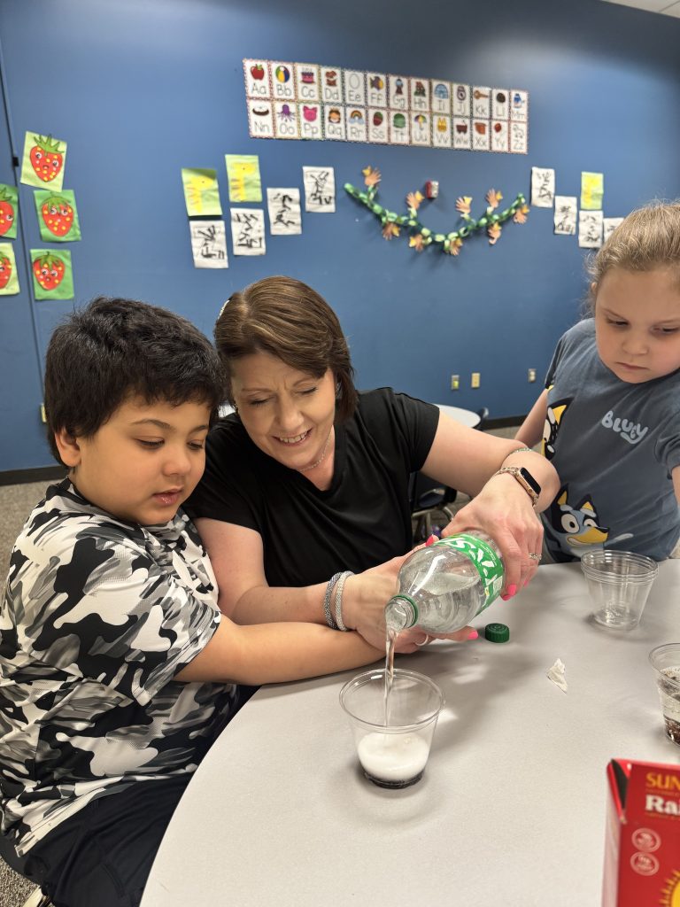 Staff member assisting a student with pouring Sprite into a cup for a dancing raisins science experiment.