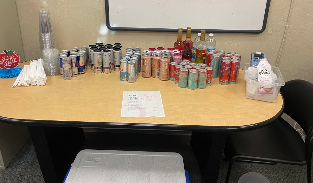 Table stocked with energy drinks and beverages beside a sign reading “Manic Monday Mocktails.”