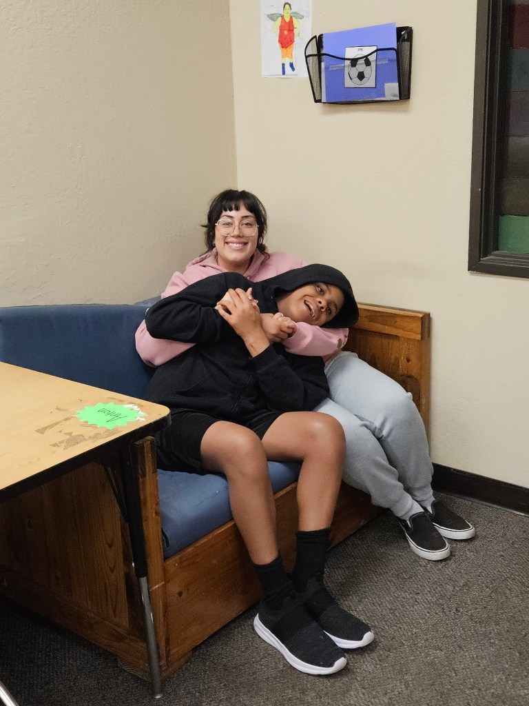 Student and staff member sharing a warm embrace in an office while smiling for the camera.