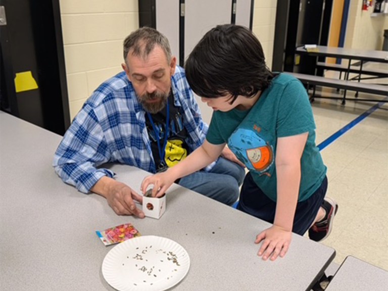 Un miembro del personal y un alumno plantan semillas juntos en una pequeña maceta hecha a mano durante una actividad con motivo del Día de la Tierra en el Northwest Center for Autism.