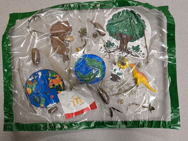 Vista aérea de un proyecto artístico dedicado al Día de la Tierra en el que se pueden ver hojas, flores, materiales reciclados, dibujos y adornos inspirados en la naturaleza.